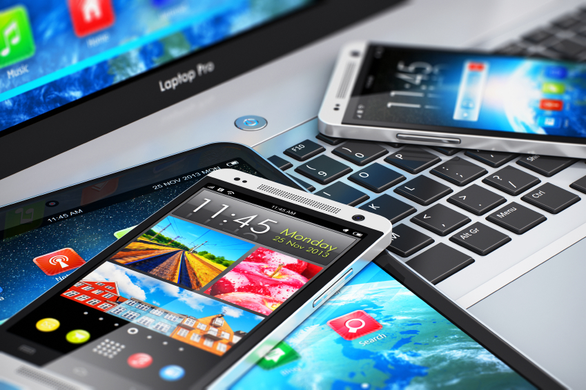 Mobility and modern internet business communication technology concept: macro view of laptop or notebook, tablet computer PC and black glossy touchscreen smartphones with color interfaces with icons and buttons